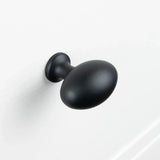 Een matzwarte, ovaalvormige Agero Black Knob Deluxe van yessential.nl is gemonteerd op een wit oppervlak.