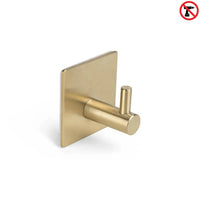 De Navarro Gold van yessential.nl is een goudkleurige, vierkante zelfklevende handdoekhaak met een cilindrische pin en een rood no-drill symbool - ideaal als handdoekhaak badkamer voor eenvoudige, boorvrije installatie.