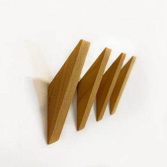Vier Fabio Beech haken van yessential.nl zijn schuin gemonteerd op een witte muur in een zigzagpatroon. Deze beukenhouten haken hebben een minimalistisch, geometrisch ontwerp en zijn gelijkmatig verdeeld.