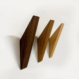 Drie Fabio Walnut houten wandhaken van yessential.nl in donker-, midden- en lichtbruin zijn diagonaal gemonteerd op een witte muur, elk met een minimalistisch ontwerp met opvallende geometrische vormen.