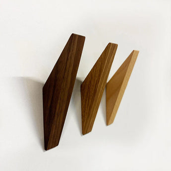 Drie Fabio Walnut houten wandhaken van yessential.nl in donker-, midden- en lichtbruin zijn diagonaal gemonteerd op een witte muur, elk met een minimalistisch ontwerp met opvallende geometrische vormen.