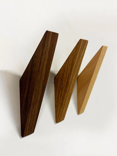 Drie Fabio Walnut houten wandhaken van yessential.nl in donker-, midden- en lichtbruin zijn diagonaal gemonteerd op een witte muur, elk met een minimalistisch ontwerp met opvallende geometrische vormen.