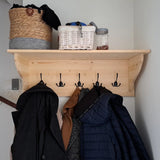 Een houten wandplank met vijf Nismo Black 2-haken van yessential.nl, waaraan jassen hangen. Op de plank staan een geweven mand, een witte mand, een grijze doek en een glazen pot - ideaal voor in de hal of entree.