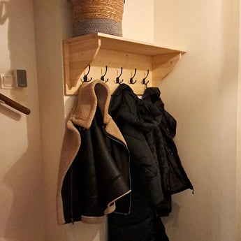 Een yessential.nl 10x Nismo Black 2-haaks wandrek houdt jassen en jacks in de gang, met een geweven mand bovenop. De schemerige verlichting creëert een gezellige sfeer.
