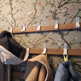 Twee Huso White kapstokken van yessential.nl zijn bevestigd aan een muur met bloemmotief. Aan de haken hangen jassen en een beige sjaal, sommige blijven leeg.