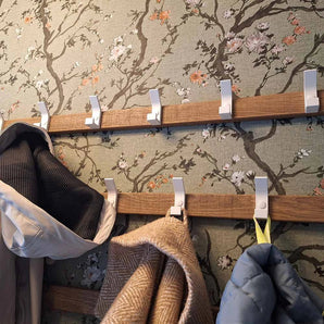 Twee Huso White kapstokken van yessential.nl zijn bevestigd aan een muur met bloemmotief. Aan de haken hangen jassen en een beige sjaal, sommige blijven leeg.