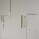 Wit gepaneelde kastdeuren met een minimalistisch geometrisch design, voorzien van elegante Remo Gold Deluxe goudkleurige handgrepen van yessential.nl voor een moderne touch.