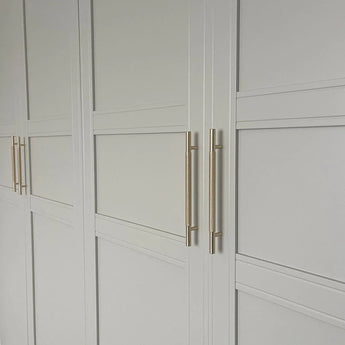 Wit gepaneelde kastdeuren met een minimalistisch geometrisch design, voorzien van elegante Remo Gold Deluxe goudkleurige handgrepen van yessential.nl voor een moderne touch.