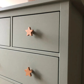 Een close-up van een grijze commode met twee lades, elk voorzien van yessential.nl Bambino Star licht houten knopjes. Deze eenvoudige, moderne commode is ideaal om charme toe te voegen aan een kinderkamer met deze unieke kinderkamer knopjes.