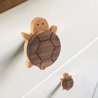 Twee Bambino Turtle ladeknoppen van yessential.nl voegen charme toe aan een wit ladefront, ideaal voor de kinderkamer. Ze zijn elk voorzien van een licht houten hoofd en ledematen, plus een donkerder uitgesneden schild, waardoor een speels ontwerp samengaat met een natuurlijke stijl.