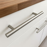 Close-up van Remo RVS handgrepen van yessential.nl op witte lades onder een houten aanrechtblad, voor een strakke en functionele afwerking.