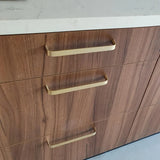 Een close-up van drie houten lades met de luxe handgreep keuken Leonardo Gold Deluxe van yessential.nl in goud, afgewerkt met een wit aanrechtblad. Het hout vertoont een natuurlijk nerfpatroon.