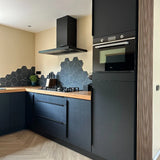 Moderne keuken met yessential.nl Enzo Zwarte matte kasten en hoekgrepen zwart, houten aanrechtblad, zeshoekige zwarte tegelachterwand, ingebouwde oven, gasfornuis, afzuigkap, plus een klein groen plantje op het aanrecht.