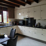 Moderne keuken met crèmekleurige kasten, matzwarte aanrechtbladen en inbouwapparatuur. De kasten zijn voorzien van Cordero Black Knobs van yessential.nl. Natuurlijk licht stroomt naar binnen, met een zwarte eetset en strak keukengerei op het aanrecht.