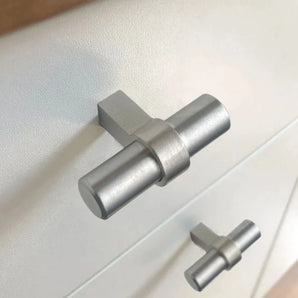 Close-up van twee moderne Arturo RVS Knopgrepen van yessential.nl op een lichtgekleurd oppervlak - de ene is scherp van voren, terwijl de andere een beetje wazig op de achtergrond lijkt.