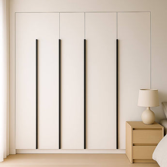 In een minimalistische slaapkamer staat de Enzo Black witte kledingkast met vier hoge zwarte profielhandgrepen van yessential.nl, een licht houten nachtkastje en een beige lamp naast een netjes opgemaakt bed met wit beddengoed.