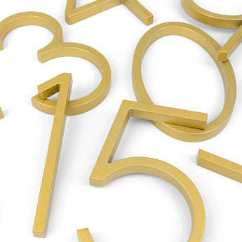 Amato Gold 12,5cm metallic cijfers van yessential.nl zijn gerangschikt op een wit oppervlak. Met strakke lijnen en een gladde afwerking, overlappen sommige in een hoek, waardoor elke entree een stijlvolle moderne look krijgt.