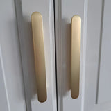 Close-up van twee verticale Arriero Gold Deluxe handgrepen van yessential.nl, gemonteerd op witte kastdeuren met een modern, minimalistisch design.