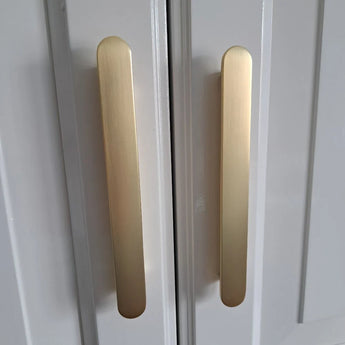Close-up van twee verticale Arriero Gold Deluxe handgrepen van yessential.nl, gemonteerd op witte kastdeuren met een modern, minimalistisch design.