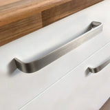 Close-up van een moderne keukenlade met Leonardo RVS Deluxe handgrepen van yessential.nl op een witte kast, met daarop een houten aanrechtblad.