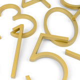 De Amato Gold 15cm huisnummers van yessential.nl (0, 1, 3, 4, 5 en 7) zijn goudkleurig en vormen samen een moderne, speelse compositie op een witte achtergrond door hun overlappende plaatsing.