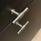 Close-up van twee Cordero RVS Knoppen van yessential.nl op donkerhouten deuren, verticaal uitgelijnd en bekeken vanuit een lichte hoek.