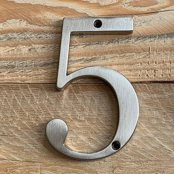 De Matteo Nickel 10cm van yessential.nl, met een geborsteld metalen afwerking, is bevestigd aan een licht houten oppervlak met twee schroeven-een boven en een onder het cijfer 5.