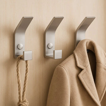 Drie yessential.nl 10x Huso RVS haken zijn gemonteerd op een beige muur: aan de linkerhaak hangt een dik touw, aan de rechterhaak een bruine jas en de middelste haak is leeg.