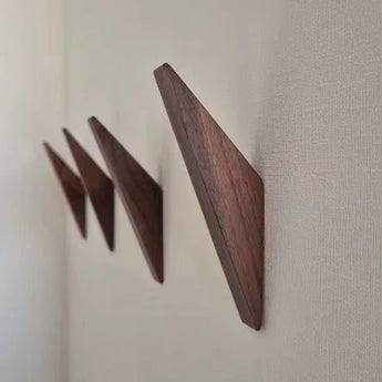 Drie Fabio Walnut haken van yessential.nl zijn in een rij gemonteerd op een lichtgekleurde muur, elk schuin omhoog om een minimalistische houten kapstok met geometrische aantrekkingskracht te vormen.