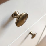 Close-up van twee Antoni Bronze meubelknoppen van yessential.nl op een witte kast. De glanzende metallic afwerking en het minimalistische ontwerp brengen een elegante stijl in elk interieur.