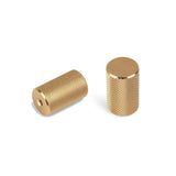 Twee Remo Gold Deluxe knoppen van yessential.nl - een paar cilindrische koperen knoppen met gestructureerde gekartelde oppervlakken, een met een gat en de andere rechtop met een gladde bovenkant - getoond op een witte achtergrond.