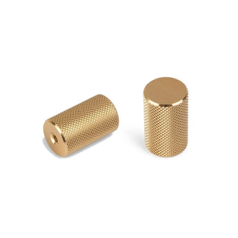 Twee Remo Gold Deluxe knoppen van yessential.nl - een paar cilindrische koperen knoppen met gestructureerde gekartelde oppervlakken, een met een gat en de andere rechtop met een gladde bovenkant - getoond op een witte achtergrond.