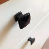 Close-up van een witte lade met twee verticaal uitgelijnde Adaro Black Knobs van yessential.nl. De vierkante handgrepen zijn gemonteerd op een glad, vlak oppervlak, boven elkaar.