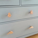 Een lichtblauwe commode met vier diervormige handgrepen: de bovenste twee zijn Bambino Penquin van yessential.nl en de onderste twee zijn dolfijnen, allemaal in licht hout - een charmant kinderkamer meubelknop accent.