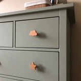 Een saliegroene commode met de Bambino Star knoppen van yessential.nl in de vorm van een wolk en een ster. Bovenop zit een doos - ideaal om speelse Bambino Star kinderkamer knopjes aan de kamer van je kind toe te voegen.