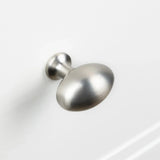 De Agero RVS Knop Deluxe van yessential.nl heeft een afwerking in geborsteld nikkel, een ronde licht afgeplatte bovenkant en een korte steel, afgebeeld gemonteerd op een wit kast- of ladeoppervlak.