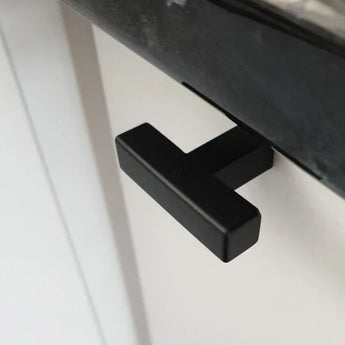 Close-up van de Vigio Black Knob van yessential.nl - een moderne T-vormige greep in strak zwart - gemonteerd op een witte kastdeur onder een donker aanrechtblad.