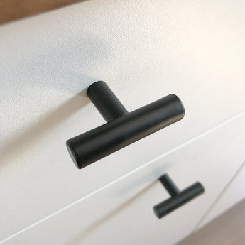 Close-up van een Remo Black knop van yessential.nl op een witte lade, met daaronder nog een identieke knop. De hoek benadrukt het moderne, minimalistische ontwerp van dit strakke beslag.