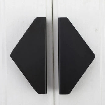 Twee zwarte, geometrische, ruitvormige boekensteunen van yessential.nl, genaamd Triano Black 64mm, staan rechtop op een wit houten oppervlak met schuine randen naar buiten en rechte randen die in het midden samenkomen.