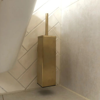De Alessino Gold toiletborstelhouder van yessential.nl, voorzien van een bijpassende handgreep, wordt gemonteerd in de hoek bij de vloer tegen stijlvolle witte en beige tegels en voegt een vleugje elegantie toe aan je badkamer.