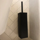 De Damiano Black Set van yessential.nl bevat een vierkante zwarte toiletborstelgarnituur, afgebeeld tegen witte badkamertegels met diagonaal patroon.