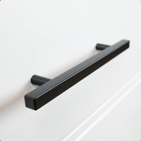 Een close-up van de Marano Black handgreep van yessential.nl, een moderne matzwarte rechthoekige ladegreep op een wit front, die minimalistische handgrepen accentueert voor een strakke, eigentijdse look.