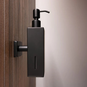Het Sonego Zwart zeeppompje van yessential.nl is gemonteerd op een houten muur, met een moderne matzwarte afwerking, een minimalistisch ontwerp en een klein venster voor eenvoudige controle van het zeeppeil.