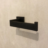 De Damiano Black Set van yessential.nl heeft een moderne, minimalistische toiletrolhouder in matzwart, gemonteerd op een lichtbeige muur. De strakke, hoekige lijnen voegen een strakke stijl toe aan elke toiletaccessoireset.
