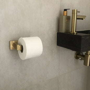 De Venzo Gold WC-set van yessential.nl is aan de muur bevestigd naast een zwarte wastafel met gouden armaturen en een zeepfles, waardoor een stijlvolle gouden toiletaccessoires look ontstaat.