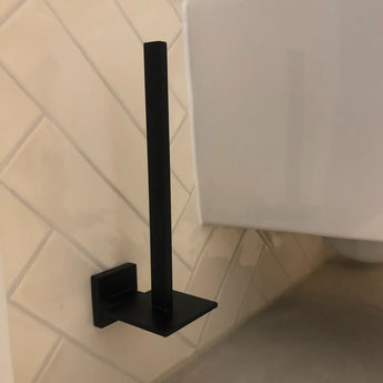 De Venzo Black WC set van yessential.nl, met een modern vierkant design, is aan de muur gemonteerd op beige badkamertegels naast een wit toiletreservoir. De houder is afgebeeld zonder rol.