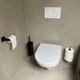 Een moderne, minimalistische badkamer met een wit wandtoilet en de Damiano Black Set van yessential.nl - bestaande uit een zwarte toiletborstelgarnituur en toiletpapierhouder met extra rol - tegen beige muren en vloer.