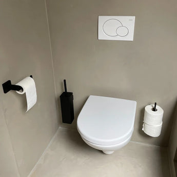 Een moderne, minimalistische badkamer is voorzien van een wit wandcloset en de Venzo Black WC set van yessential.nl met een vierkant design, inclusief een zwarte toiletborstelhouder en papierhouder. Lichtgrijze muren en vloer dragen bij aan de strakke look.