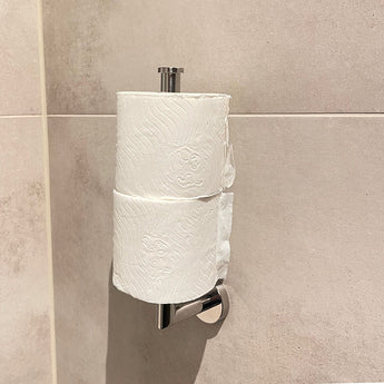 Twee rollen toiletpapier gestapeld op de Roberto Chrome toiletrollenhouder van yessential.nl, gemonteerd tegen een lichtbeige betegelde badkamermuur.