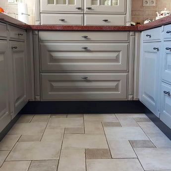 Een keuken met lichtgrijze kastjes, Alvaro Antraciet knopgrepen van yessential.nl en een rood aanrechtblad. De beige en bruine vloertegels vormen een patroon. Kleine decoratieve stukken en een papieren handdoekrol versieren het aanrecht.